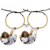 Zwei stilvolle Armbänder mit goldenen Perlen und schwarzer Kordel, die jeweils eine personalisierbare Fotolinse enthalten. Beide Armbänder sind mit einem herzförmigen Anhänger verziert, der in der Mitte geteilt ist und sich magnetisch zusammenhält. Die Fotolinsen zeigen das Bild eines fröhlichen Paares, das gemeinsam lacht. Der schlichte, weiße Hintergrund lässt die Armbänder und die lebhaften Bilder besonders gut zur Geltung kommen.