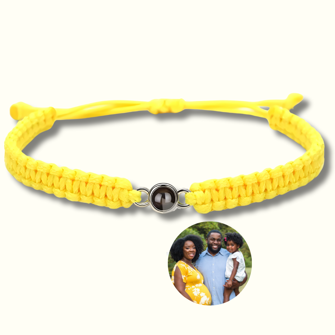 Gelbes Makramee-Armband mit Fotoperle / Fotolinse in der Mitte. Beispielprojektion zeigt eine glückliche Familie mit einem schwangeren Paar und ihrem kleinen Kind. Heller Hintergrund.