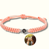 Rosa Makramee-Armband mit Fotoperle / Fotolinse in der Mitte. Beispielprojektion zeigt eine Mutter, die ihr kleines Kind küsst. Heller Hintergrund.