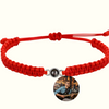 Rotes Makramee-Armband mit silbergerahmter Fotoperle / Fotolinse in der Mitte. Beispielprojektion zeigt einen Gitarristen beim Spielen der Gitarre. Heller Hintergrund.