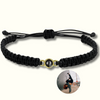 Schwarzes Makramee-Armband mit goldgerahmter Fotoperle / Fotolinse in der Mitte. Beispielprojektion zeigt eine Person, die einen Handstand macht. Heller Hintergrund.