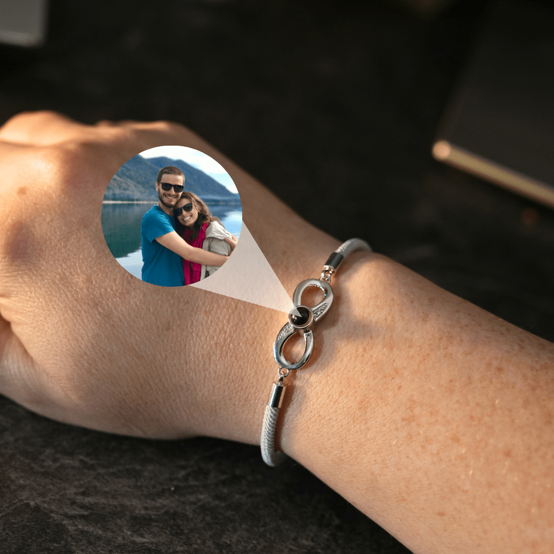 Ein Paar steht vor einer malerischen Seeuferkulisse, wobei der Arm der Person ein silbernes Infinity-Armband mit einer Fotolinse zeigt, die ein Bild des Paares enthält.